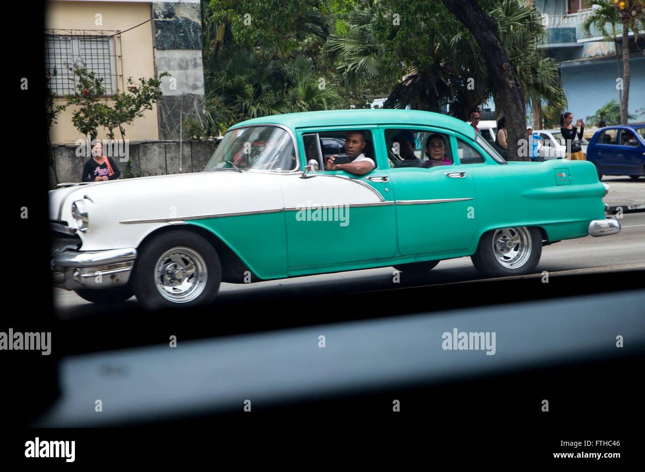 A vintage American car driven by a Cuban family watches as the motorcade of U.S President Barack Obama drives past during his historic visit to the island nation March 20, 2016 in Havana, Cuba. Stock Photo