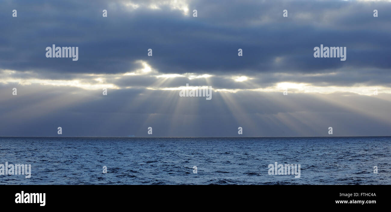 Crepuscular rays appear as the sun breaks through broken cloud above the Southern Ocean near the South Orkney Islands. Stock Photo