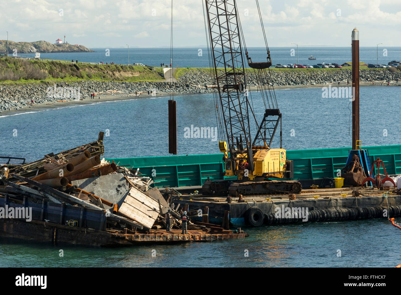 Beached stranded barge with load of junk being unloaded by large crane at Clover Point beach-Victoria, British Columbia, Canada. Stock Photo