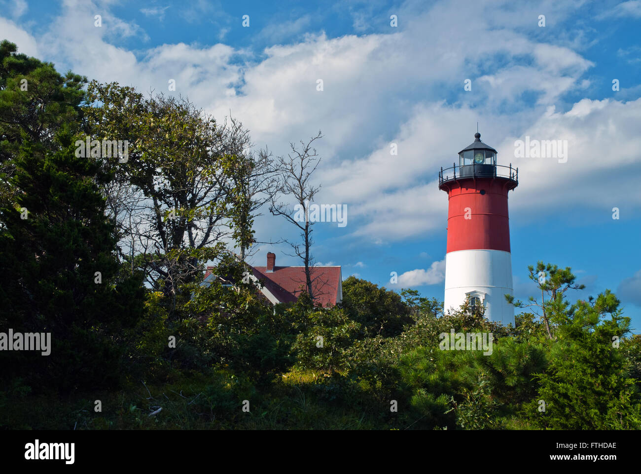 Nauset lighthouse lantern still shines on a sunny summer day with clouds. It has a unique red and white striped tower. Stock Photo