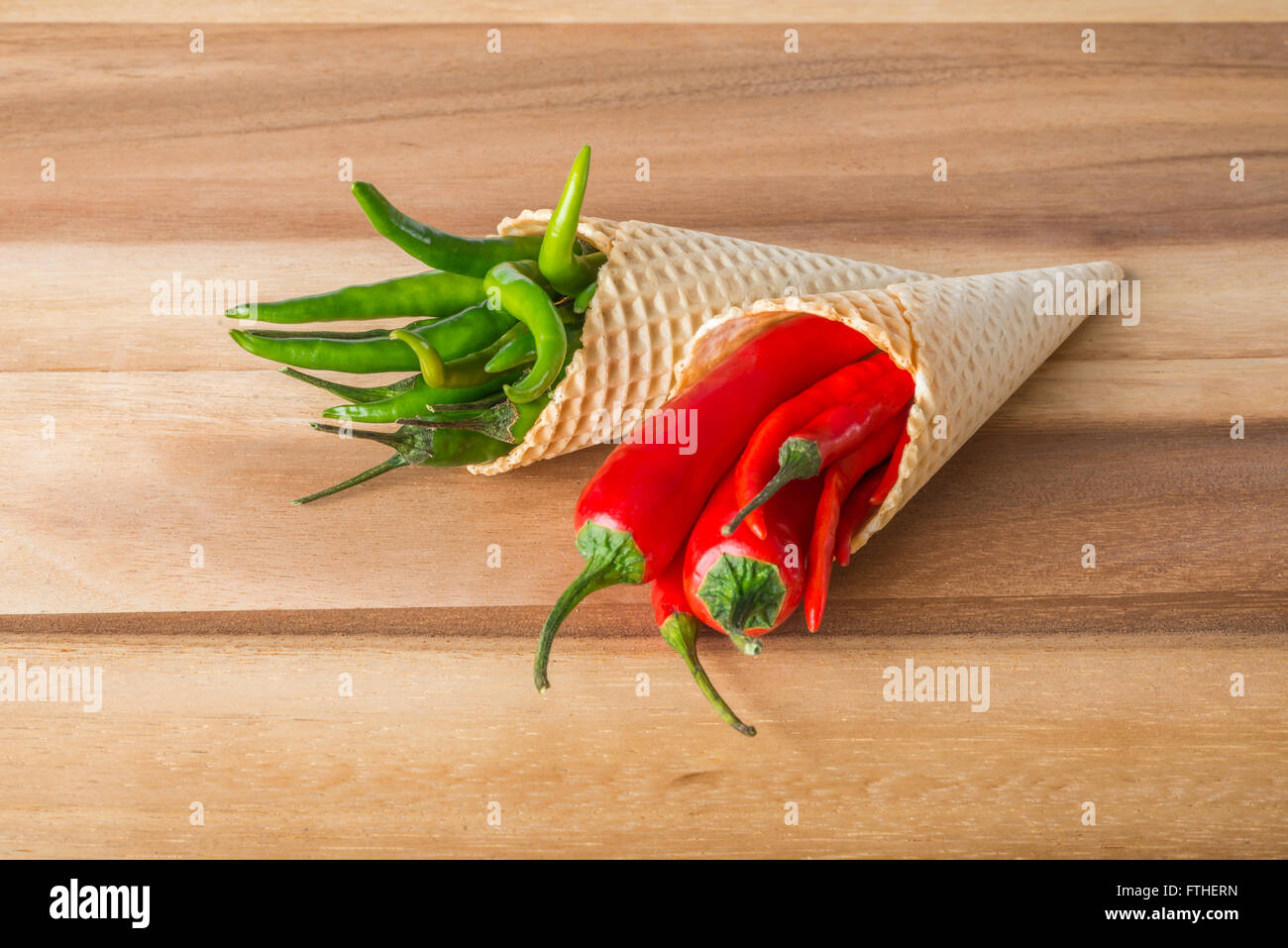 Red and green hot chili peppers in wafer cones on wooden background Stock Photo