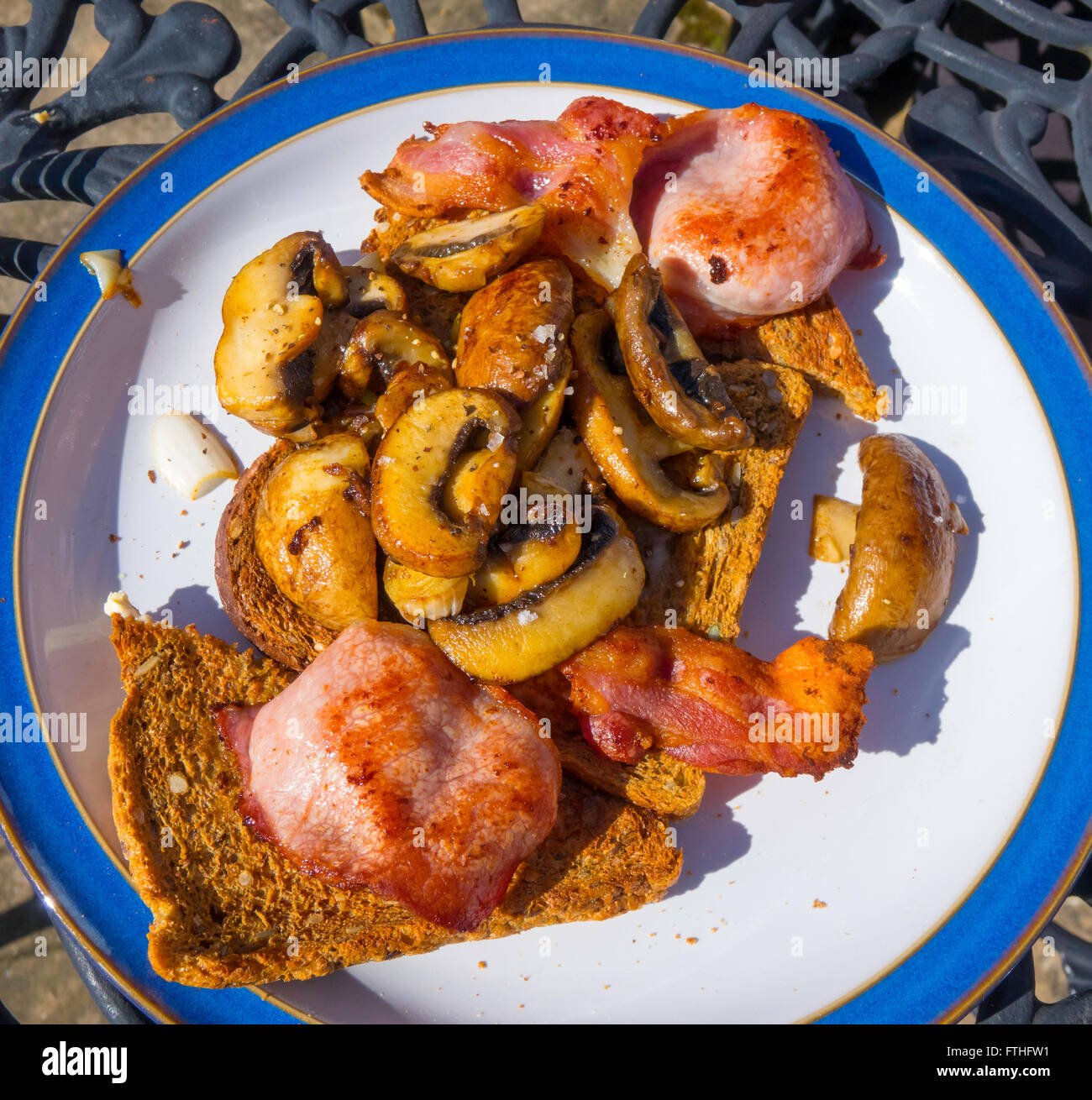 Lunch served on a garden table toasted multigrain bread with fried bacon and mushrooms Stock Photo