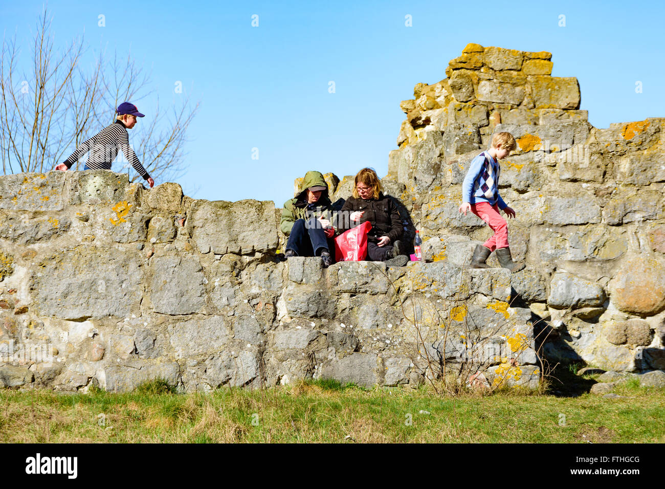 Ahus, Sweden - March 20, 2016: Young people resting and having fun at a stone ruin. Two adults sit and talk while two kids run a Stock Photo