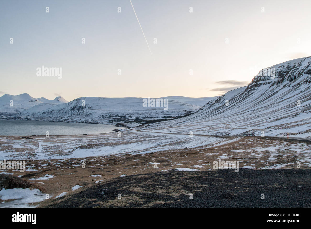 Snowy mountains across Hvalfjordur in winter at sunrise with streaks in clear sky Stock Photo