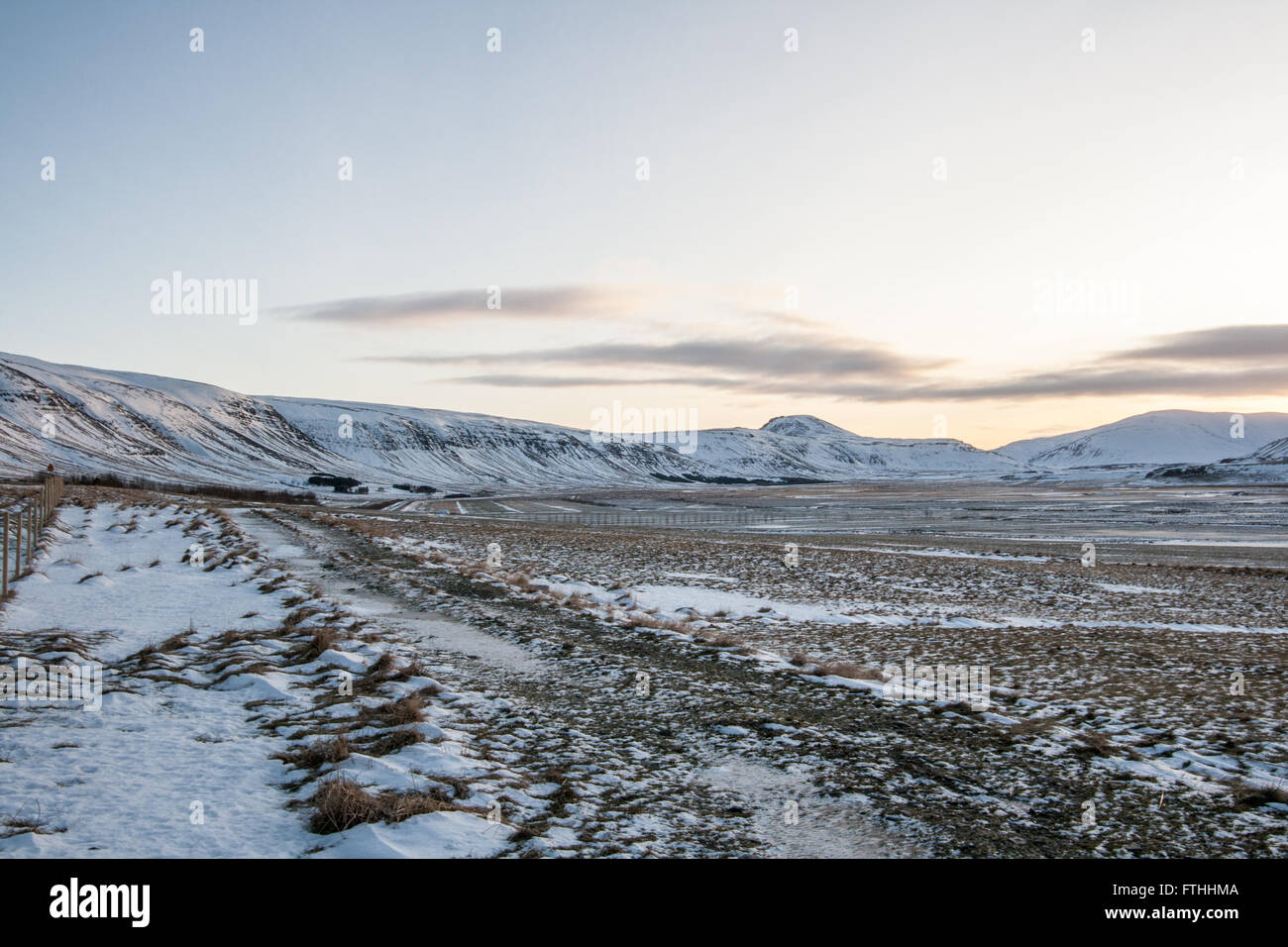 Snow covered field surrounded by snowy mountains with a clear sky at sunrise in Iceland Stock Photo