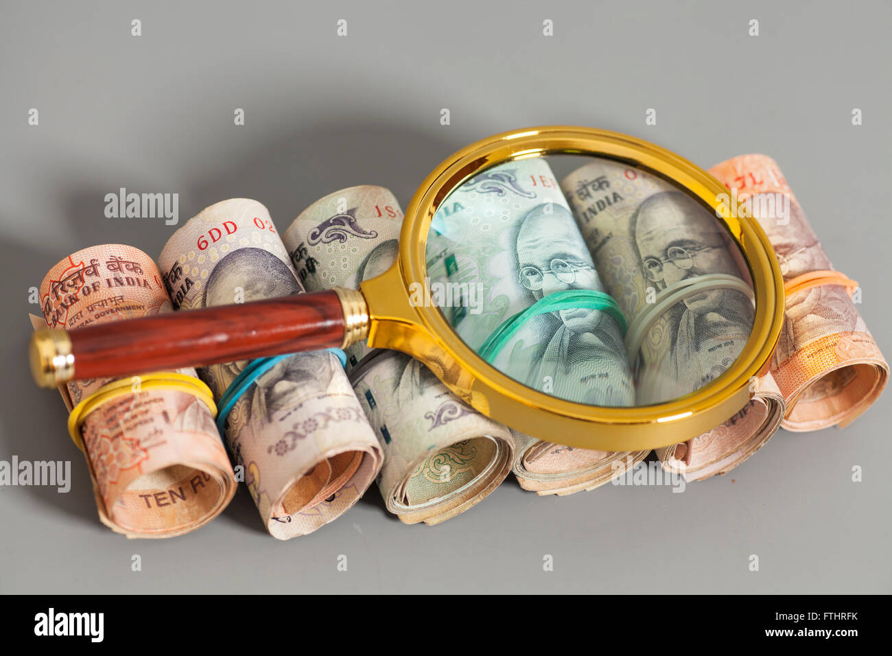 Rolls of Indian Currency Rupee Notes with magnifying glass on gray ...