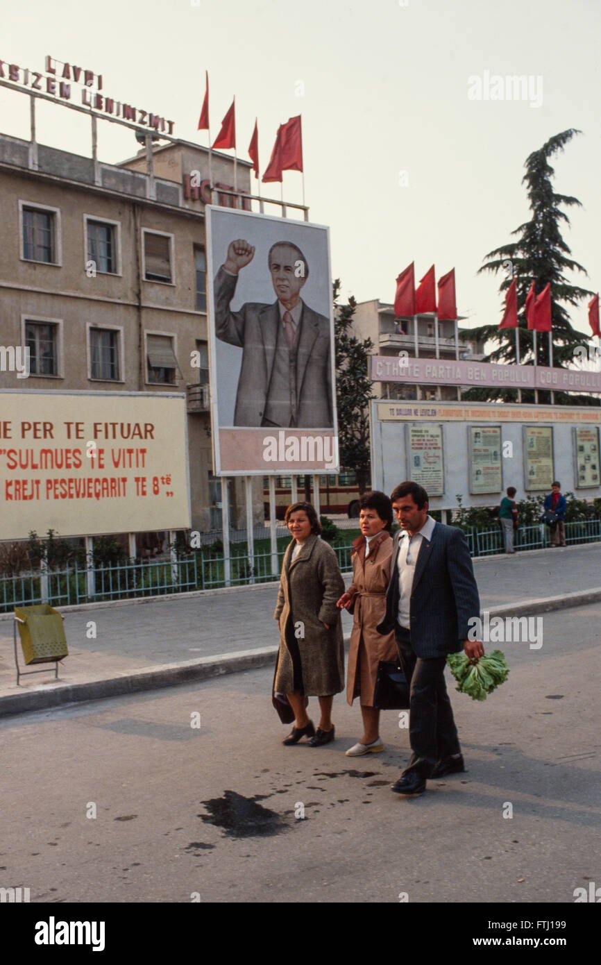People walk past the communist party slogans outside the tourist hotel  in the coastal town of Vlore. Stock Photo
