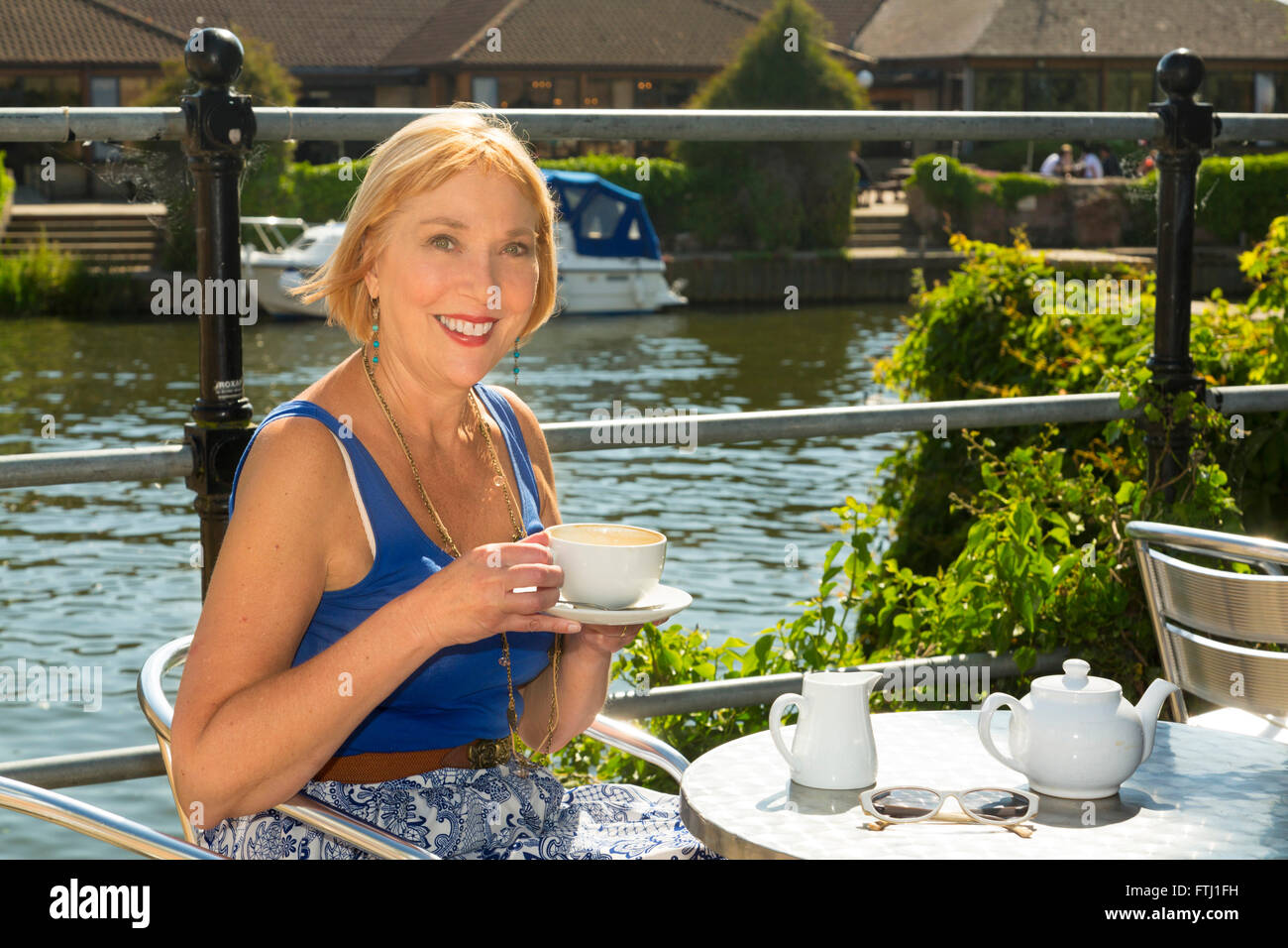 woman drinking cup of coffee outdoors next to a river Stock Photo
