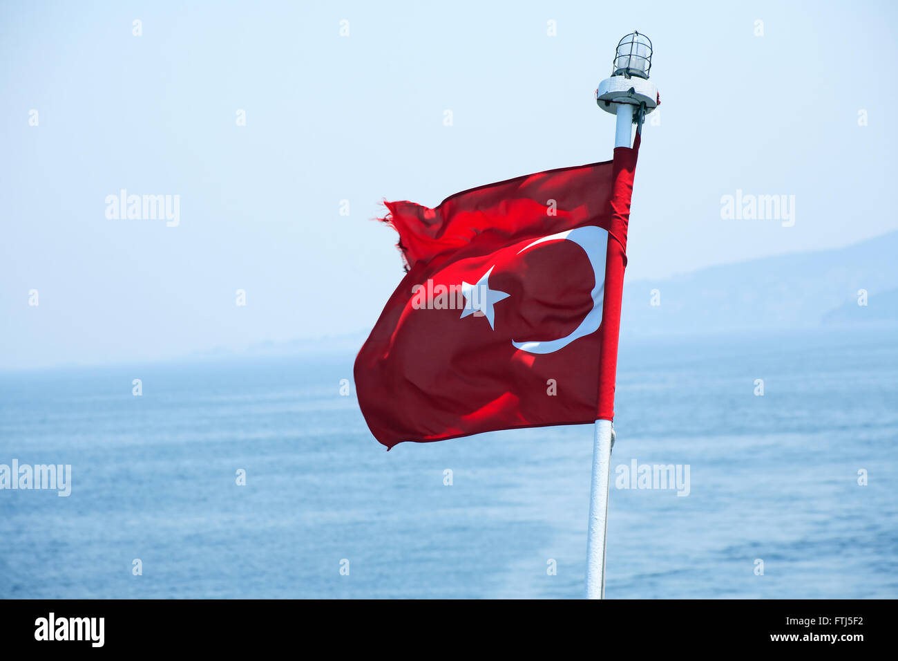 Turkish state flag waving on blue background with sea and sky Stock Photo