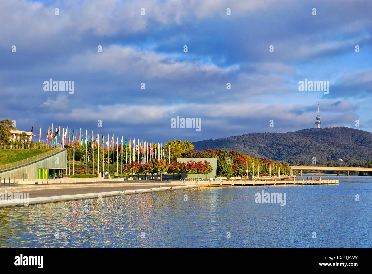 autumn trees on a wateredge of Lake Burley Griffin in Canberra under warm morning sun with Flags in background. Stock Photo