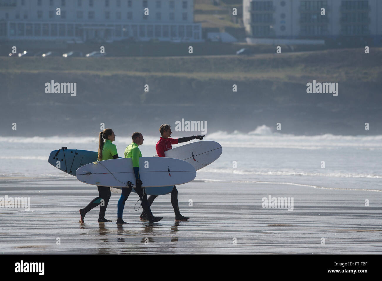 A surfing instructor and his two novices carrying their surfboards on Fistral Beach in Newquay