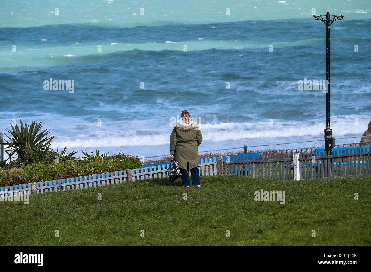 A woman stands alone looking out over the sea at Towan Beach in Newquay, Cornwall. Stock Photo