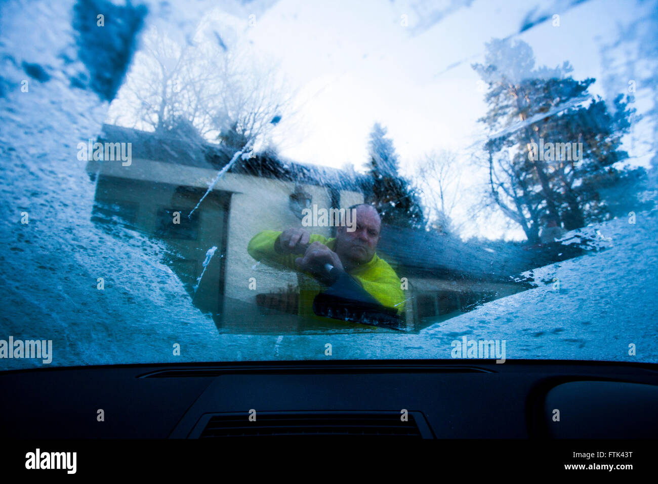 Person scraping ice off windscreen with camera placed inside car looking out towards person scraping, Flintshire, Wales, UK Stock Photo
