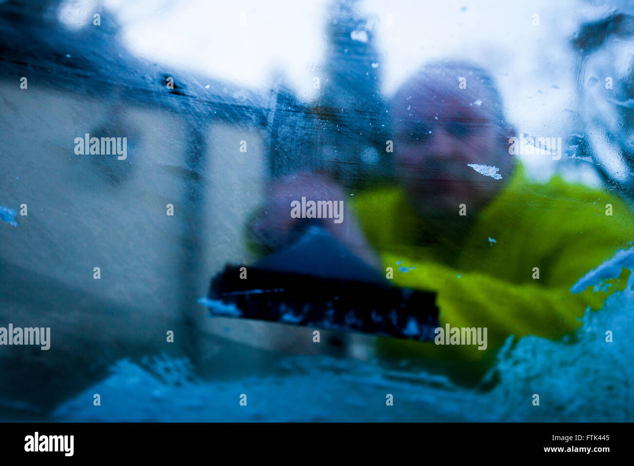 Person scraping ice off windscreen with camera placed inside car looking out towards person scraping, Flintshire, Wales, UK Stock Photo
