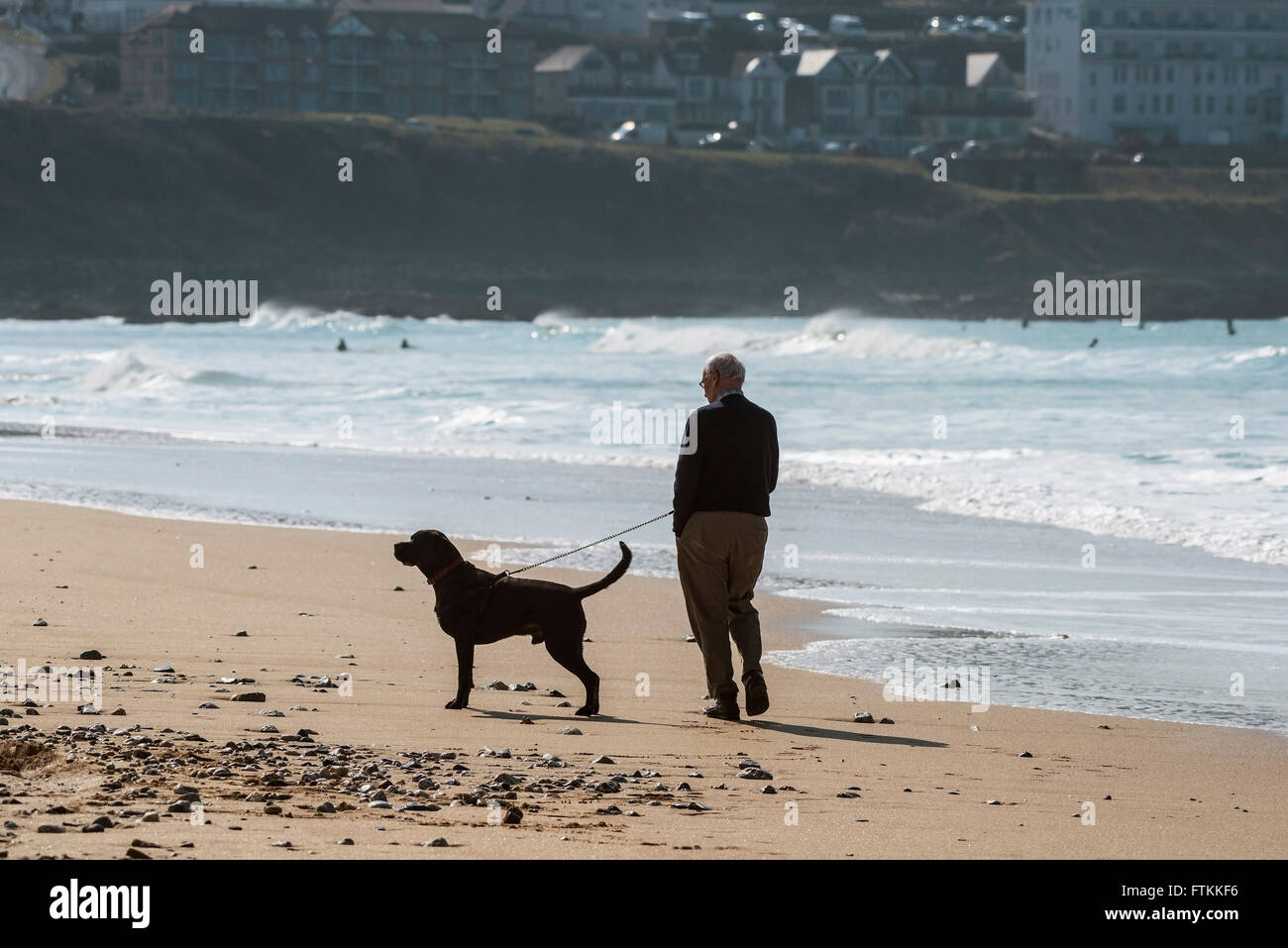A man walks his dog on Fistral Beach in Newquay, Cornwall. Stock Photo