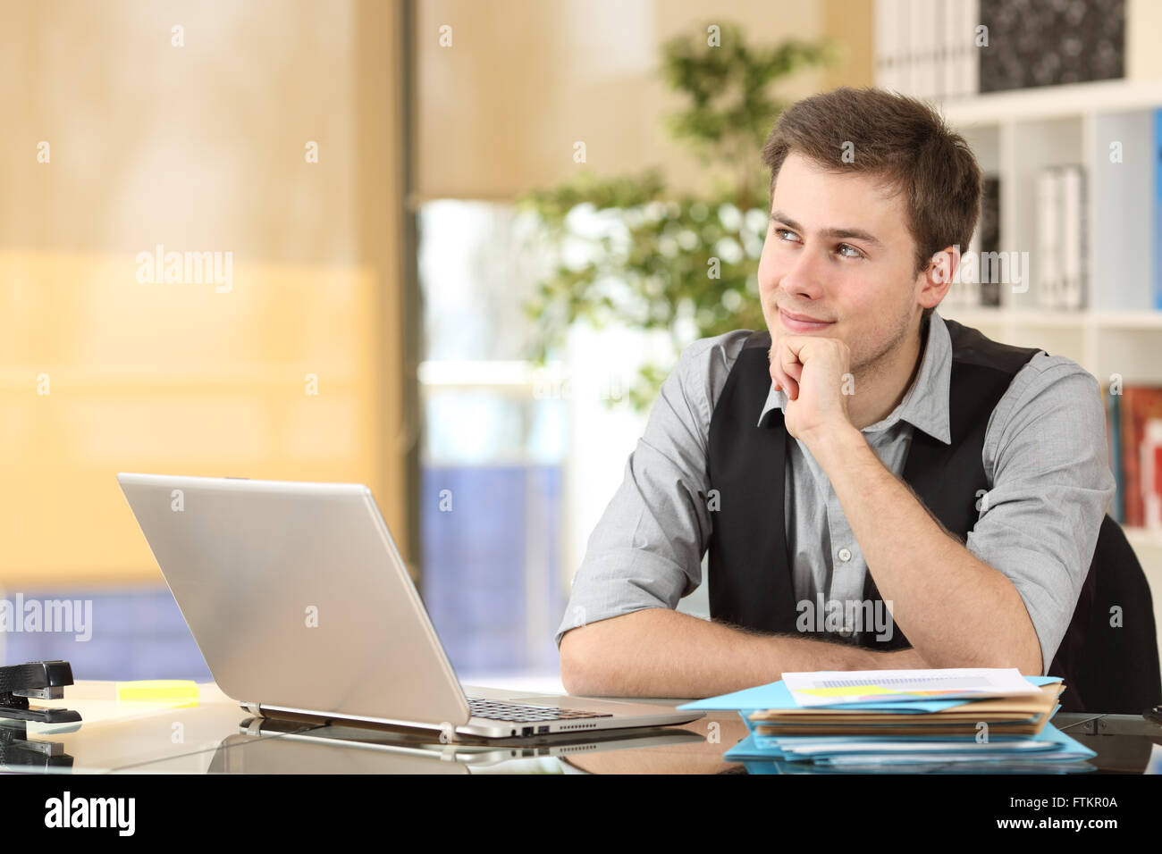 Businessman thinking and planning looking sideways sitting in a desktop with an office background Stock Photo