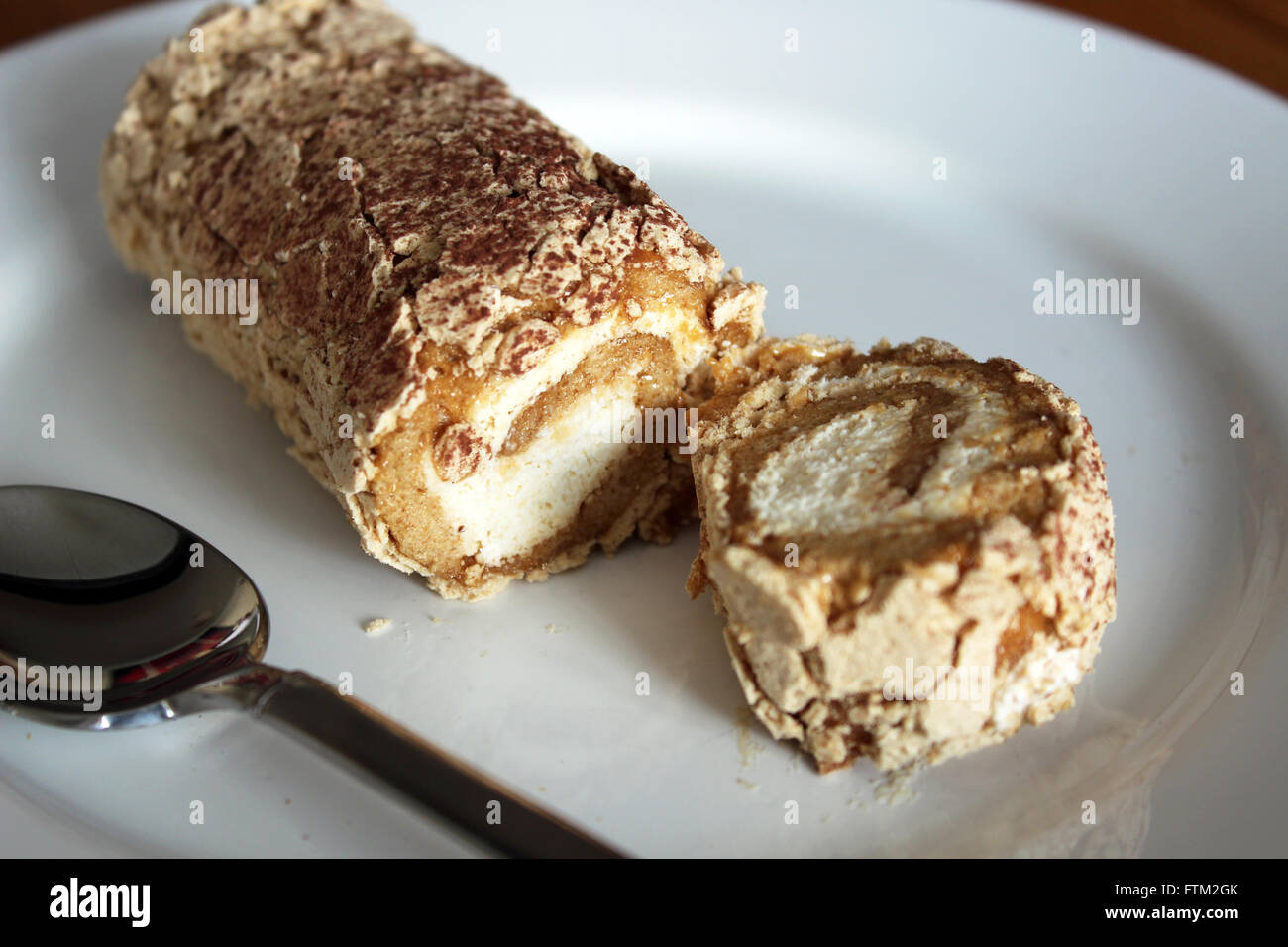 A Toffee Roulade displayed on a white plate served with a spoon ready to eat Stock Photo