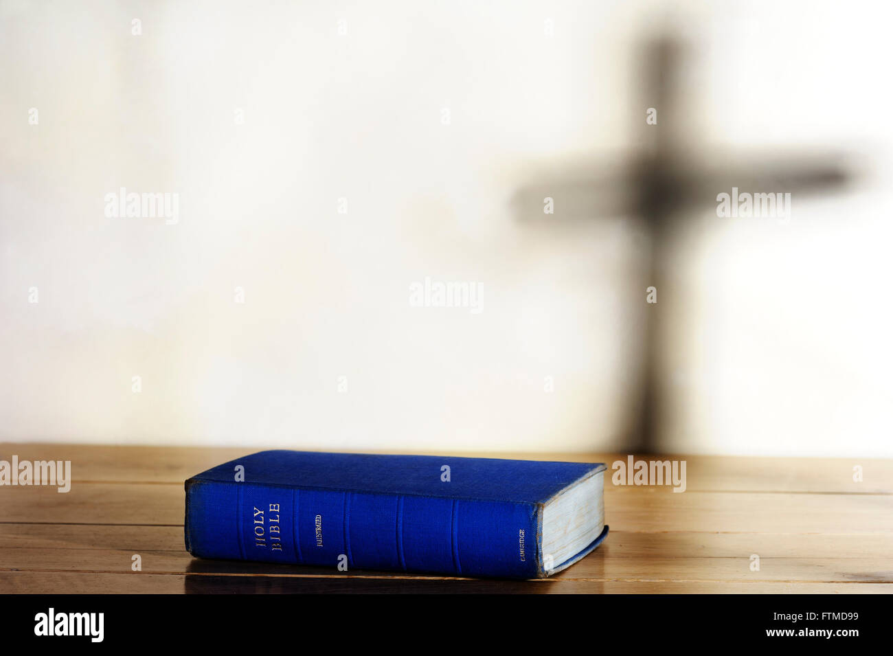 Old copy of Holy Bible lying on a table with shadow of a cross on background. Stock Photo