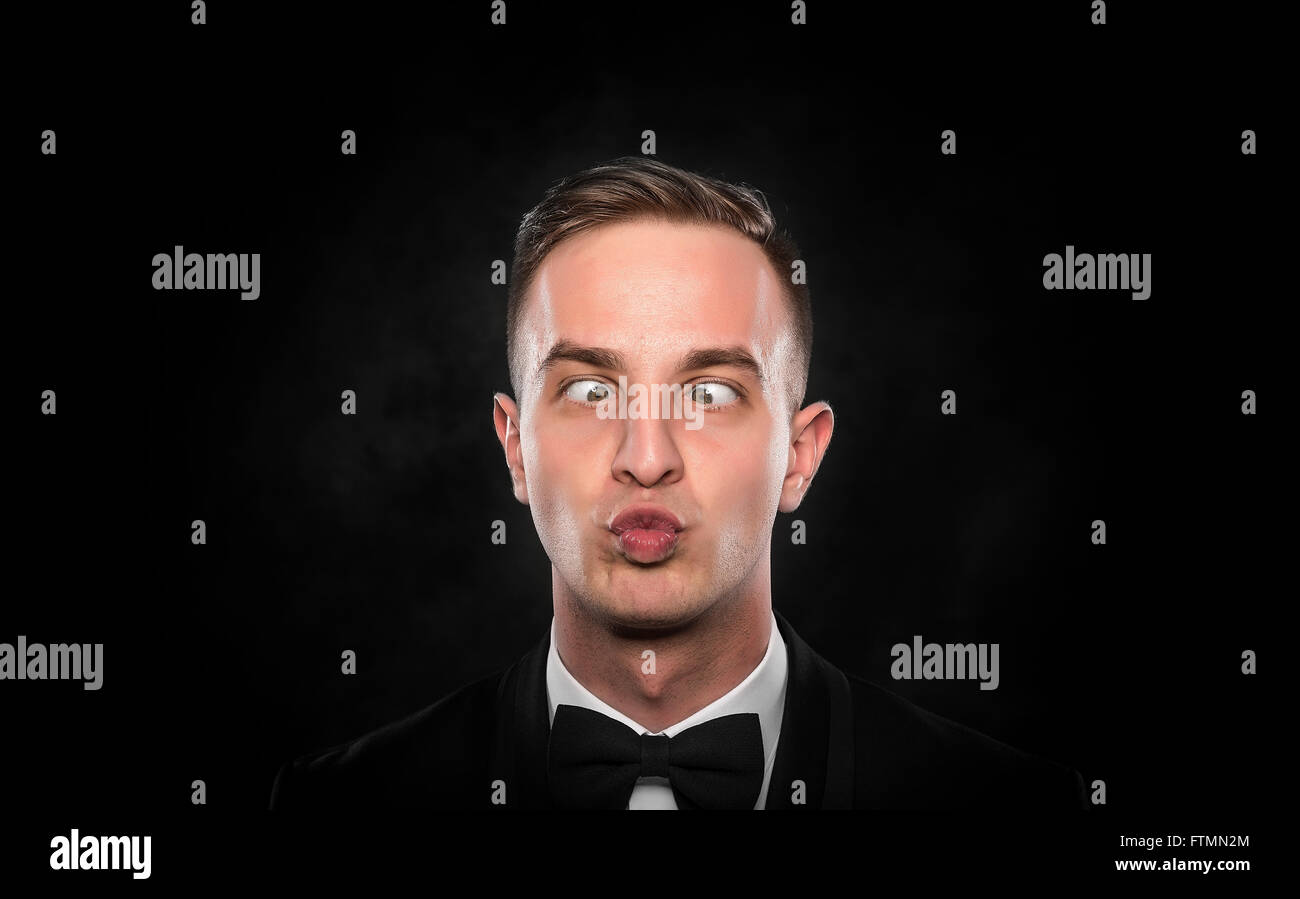 Portrait of a young cross-eyed businessman with funny face over dark background. Stock Photo