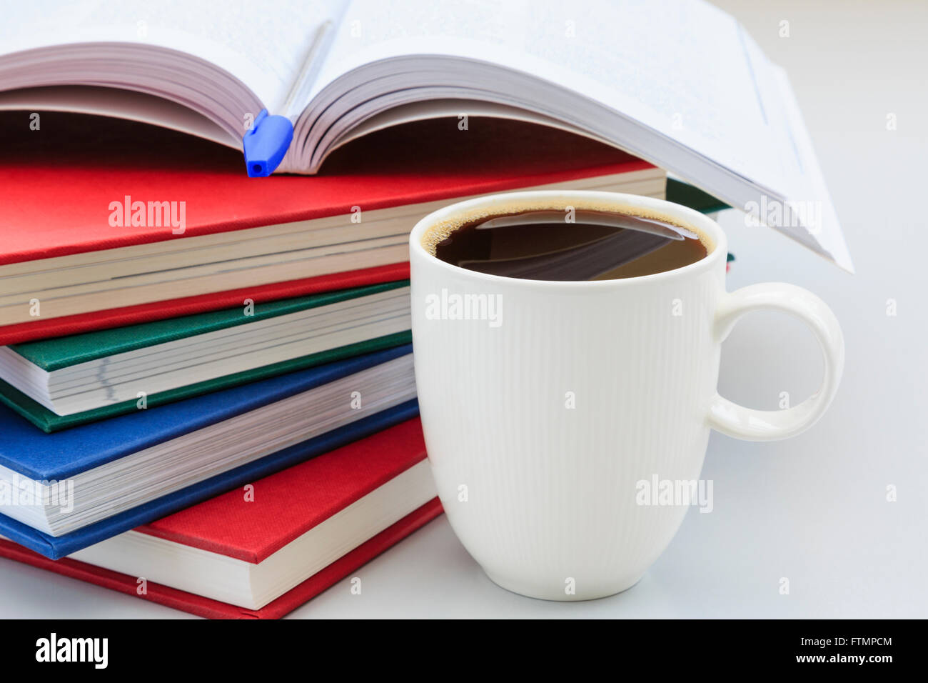 Student's study scene with pile of books on a desk with a mug of strong black coffee to help stay awake for revising studying. England UK Britain Stock Photo