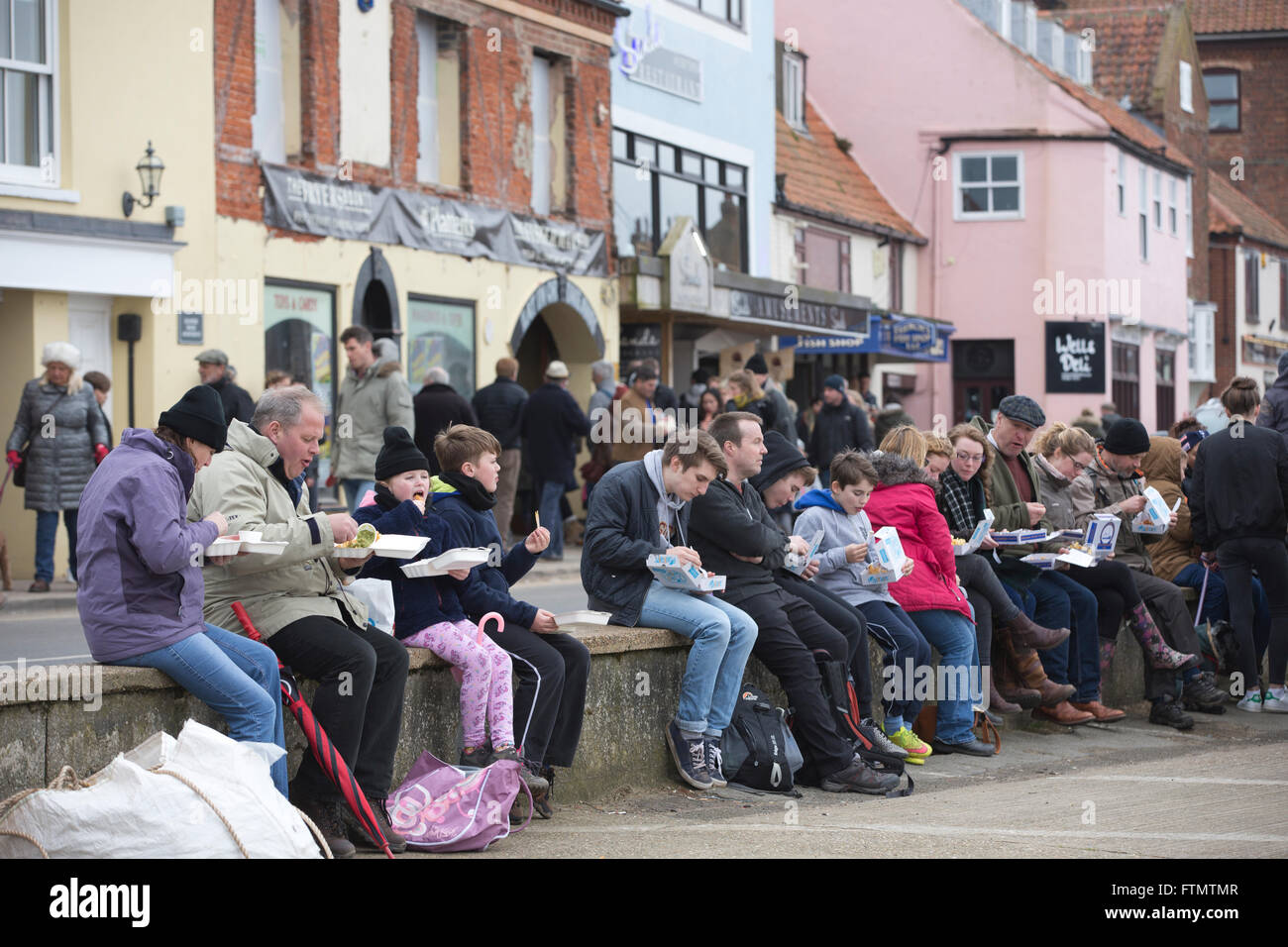 People sat along Wells-next-the-sea harbour wall eating take-away fish and chips, Norfolk coastline, East Anglia, England, UK Stock Photo