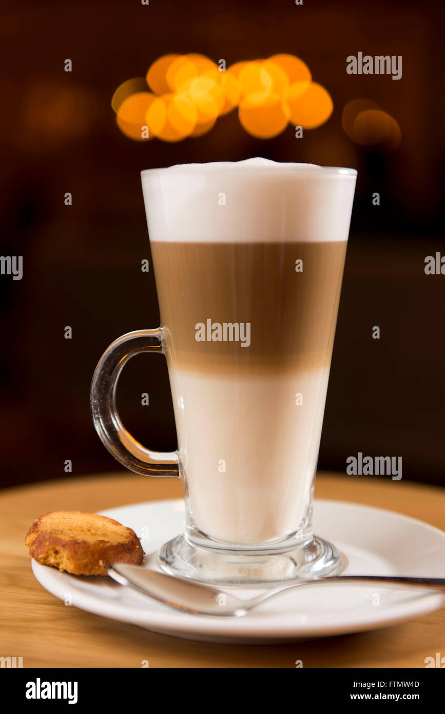 Caffe macchiato coffee drink in a long glass served in a coffee shop on a saucer with a biscuit. Stock Photo