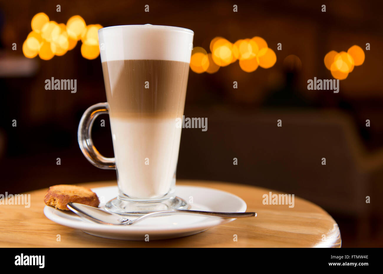 Caffe macchiato coffee drink in a long glass served in a coffee shop on a saucer with a biscuit. Stock Photo