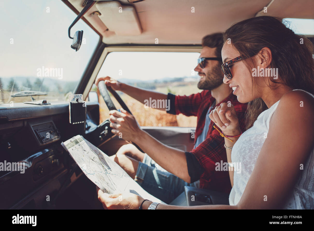 Side view of young couple using a map on a roadtrip for directions. Young man and woman reading a map while sitting in a car. Stock Photo