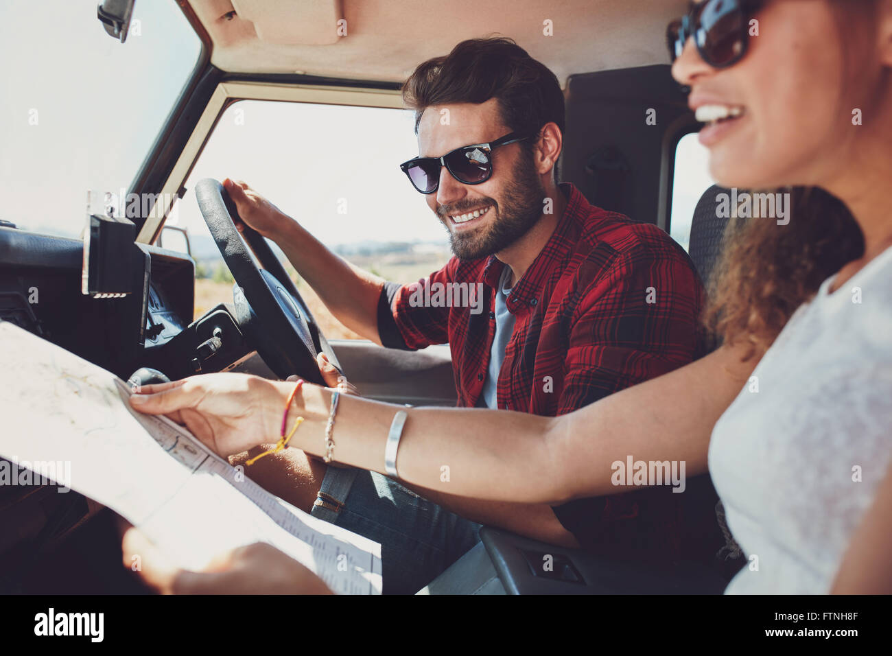 Smiling young man driving the car with woman holding a road map. Young couple on road trip. Stock Photo