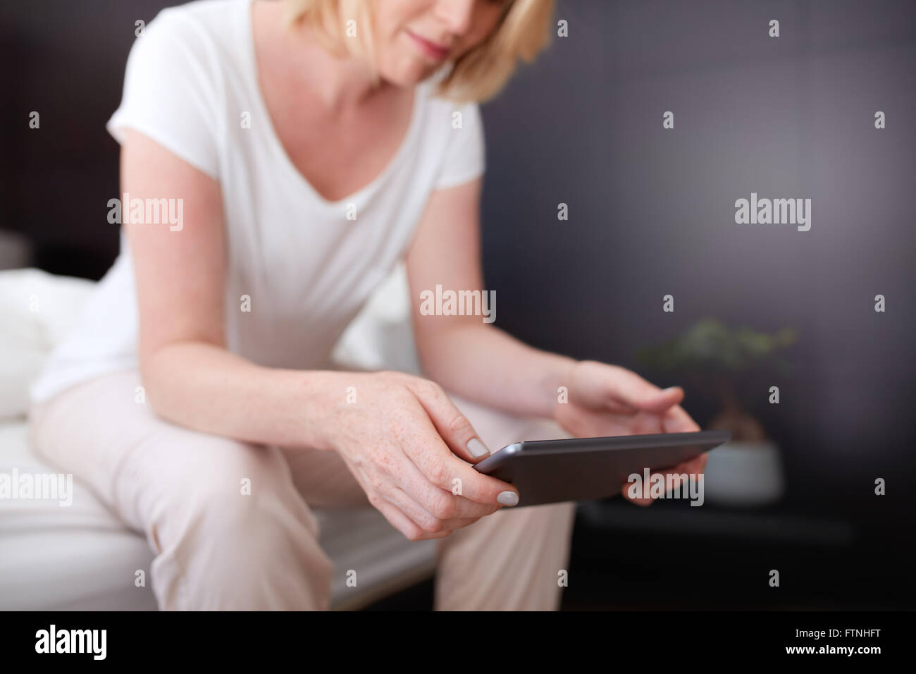 Cropped shot of a woman using digital tablet while sitting on the edge of bed. Focus on tablet  pc and woman hands. Stock Photo