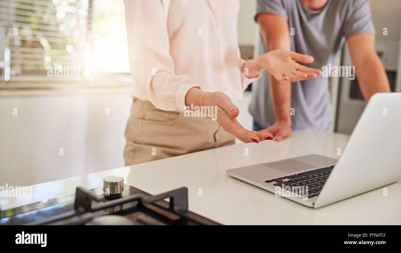 Cropped shot of couple working together on a laptop in the kitchen. Couple standing by the kitchen counter, with woman explainin Stock Photo