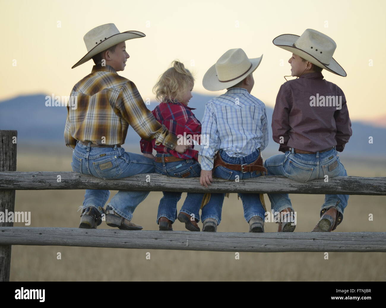 Cowboy kids sitting on old wooden fence with cowboy hats on. Stock Photo