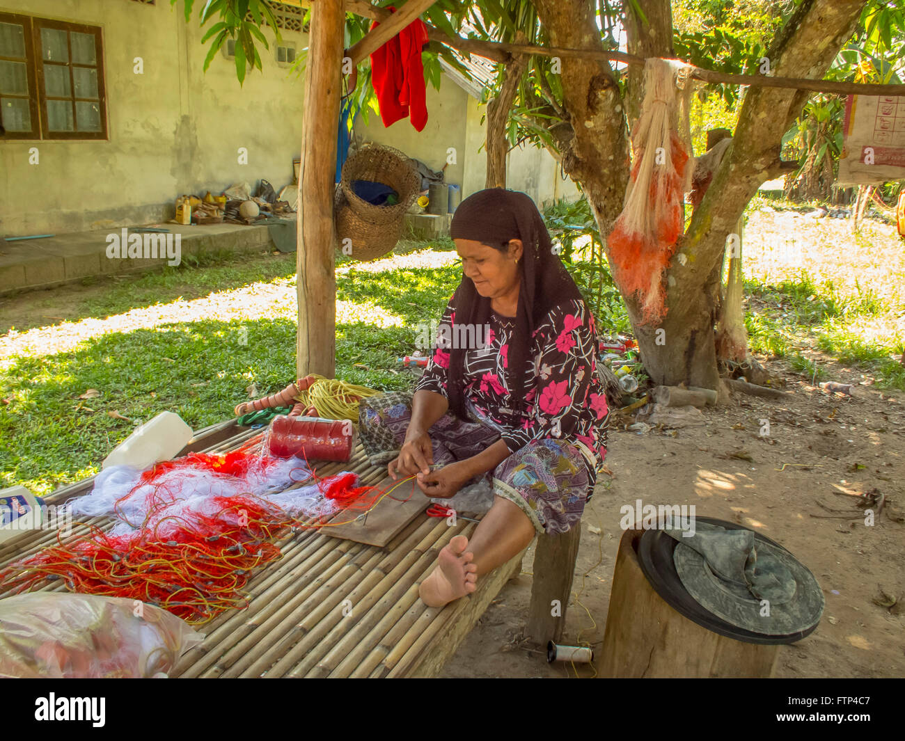 Kho Yao Yai island local woman in traditional costume repairs a fishing net on a bench. Stock Photo