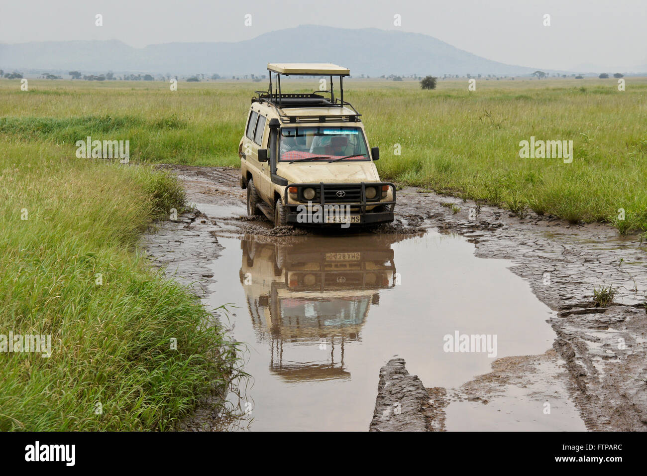 Safari vehicle driving through a mud hole on the Serengeti, Tanzania Stock Photo