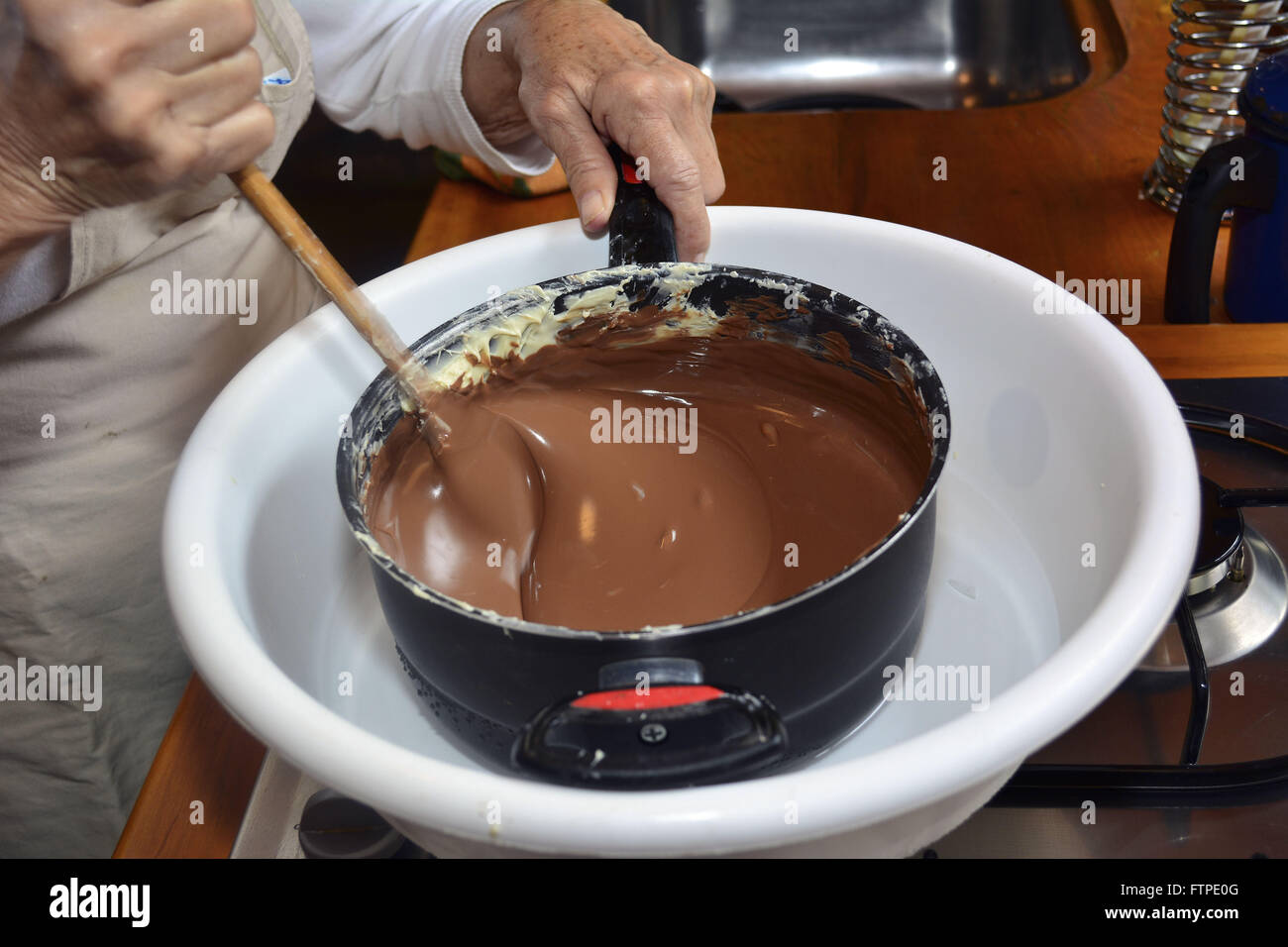 Woman melting chocolate in a double boiler for production of handmade Easter eggs Stock Photo
