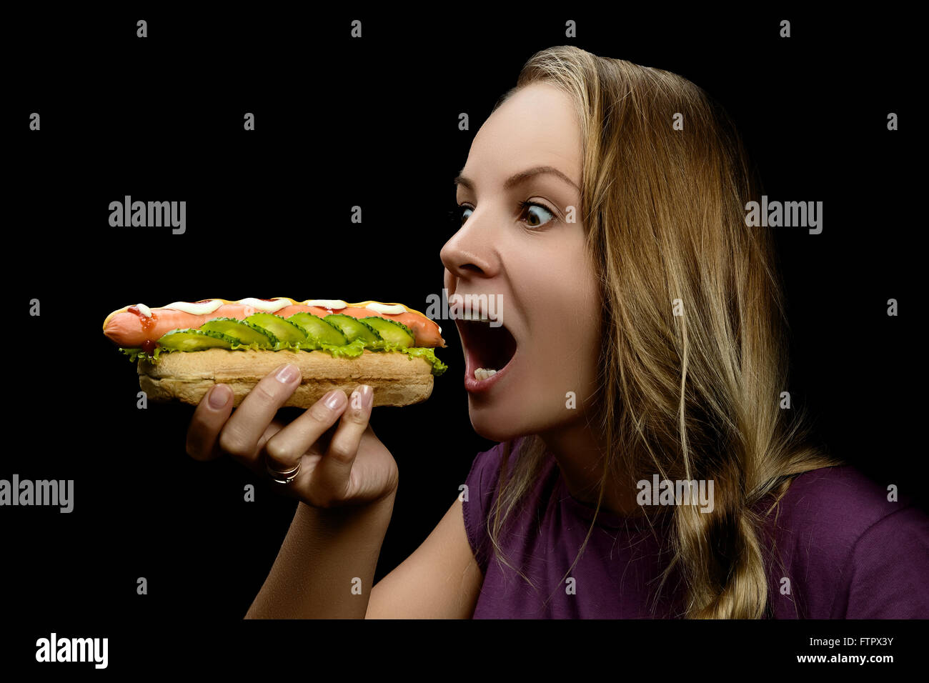 Young pretty girl eating a messy hotdog isolated on black background Stock Photo