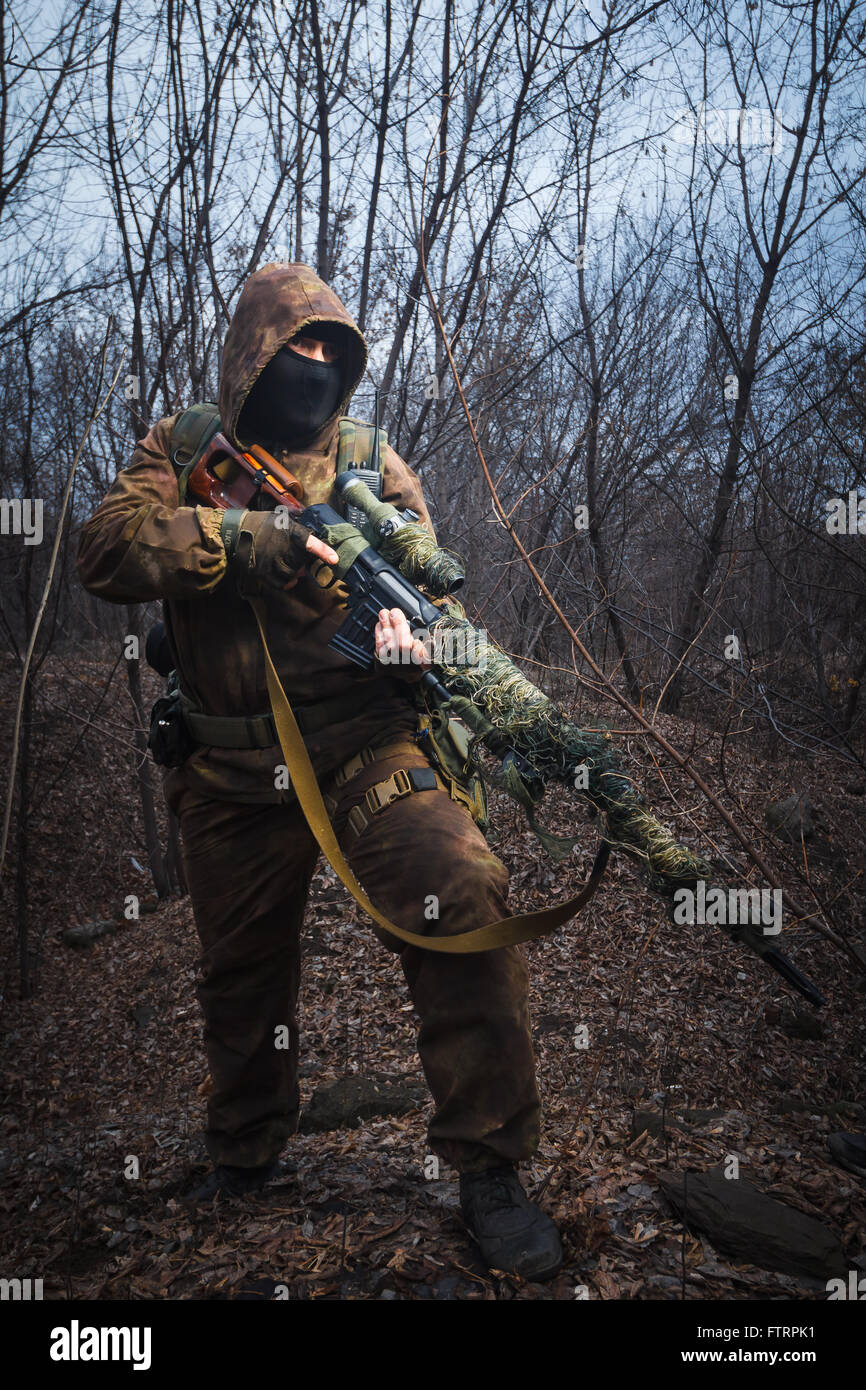 Sniper wearing camouflage suit with rifle walk in the woods Stock Photo