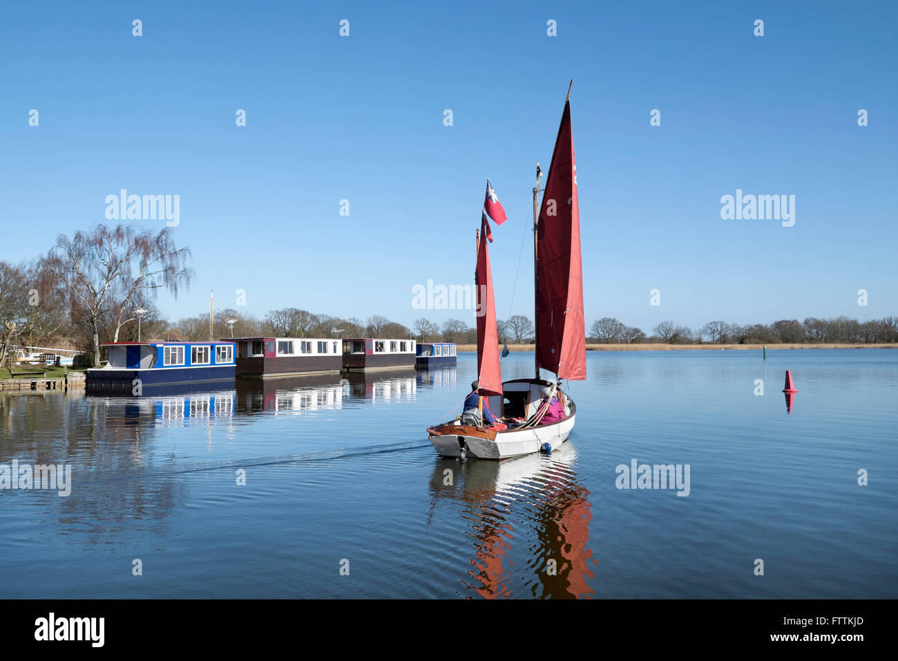 A traditional sailing dinghy sails past a row of houseboats on Hickling Broad, Norfolk, England, UK Stock Photo