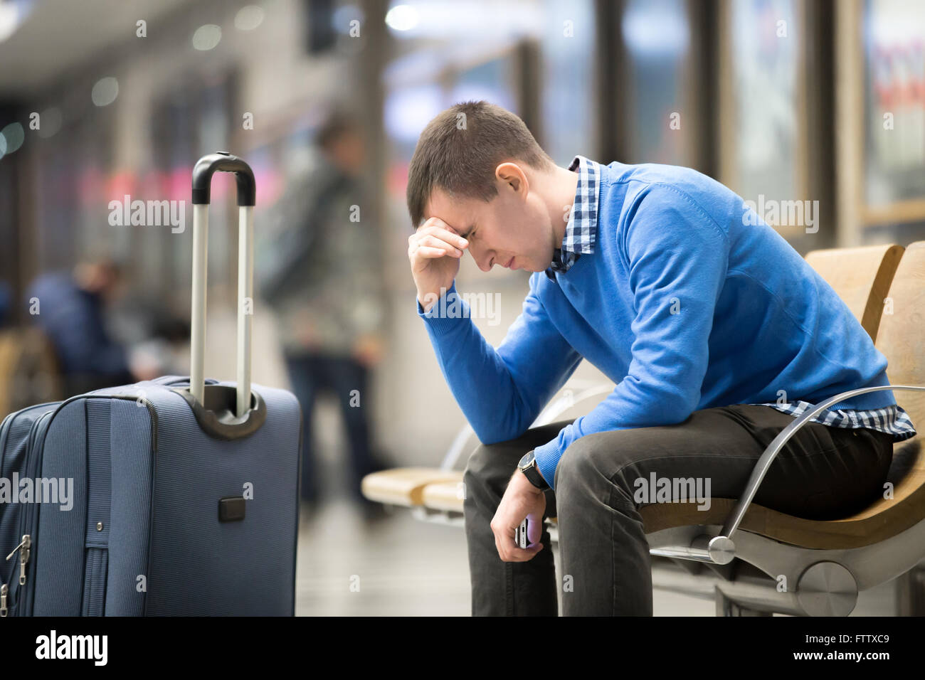Portrait of young handsome guy wearing casual style clothes waiting for transport. Tired traveler man travelling with suitcase Stock Photo