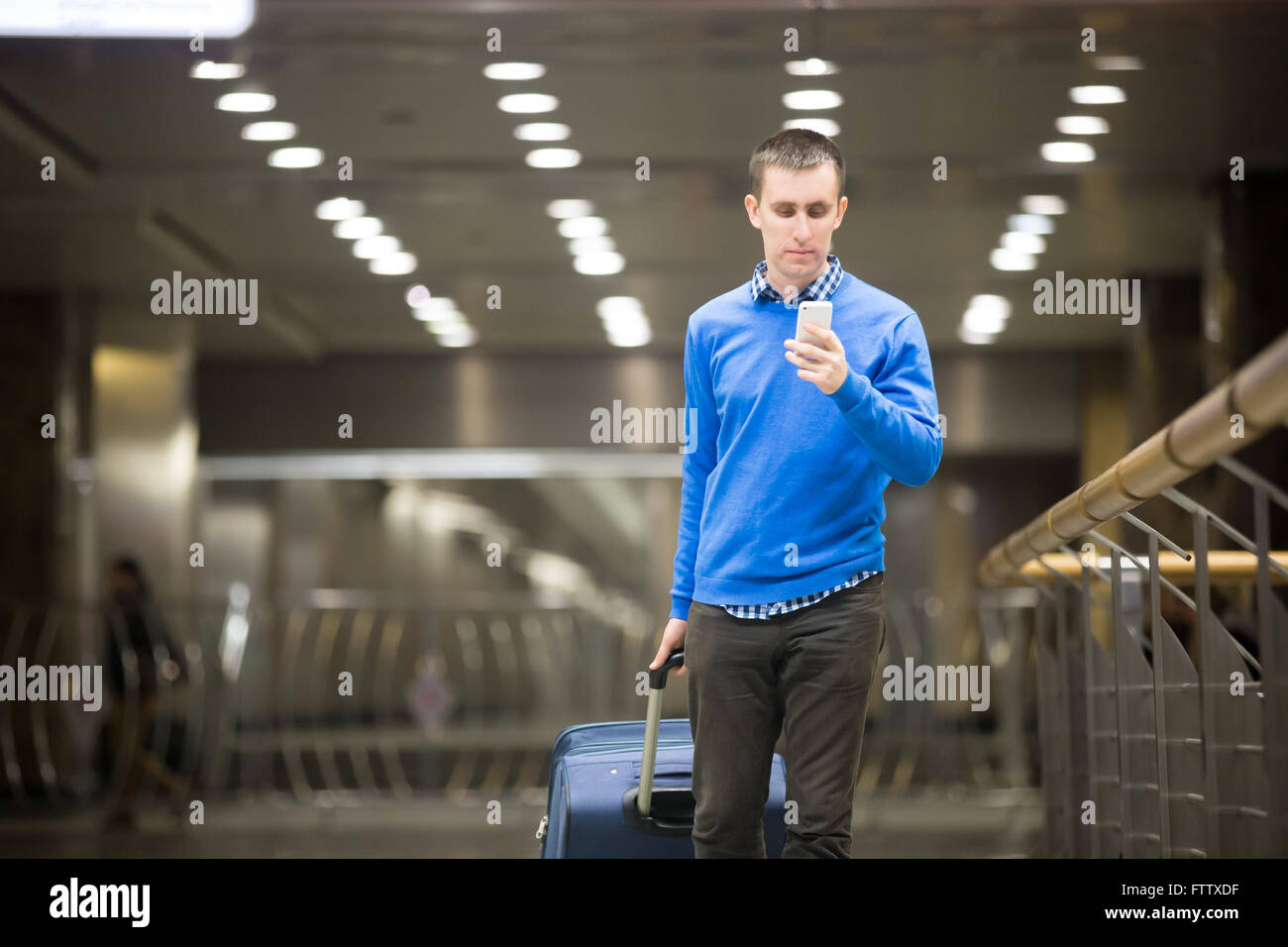 Portrait of young handsome guy wearing casual style clothes walking in modern station. Traveler making call using smartphone Stock Photo
