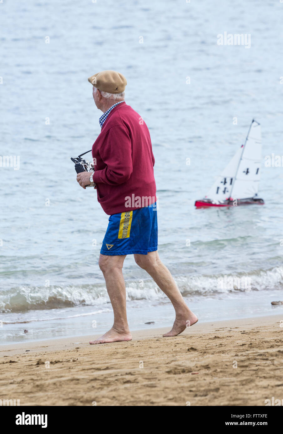Elderly men in Spain walking along beach controlling radio controlled yacht. Stock Photo