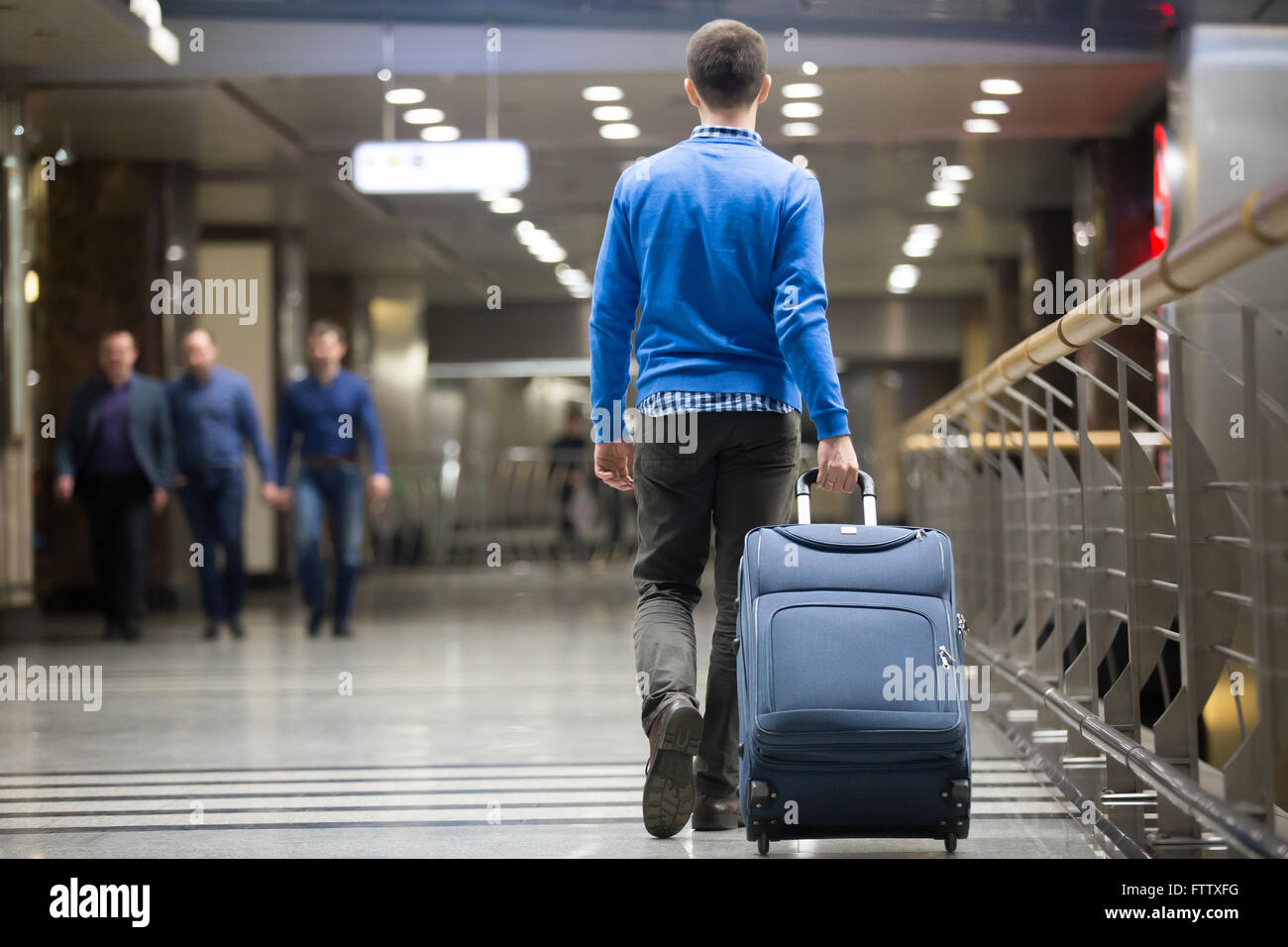 Young man pulling suitcase in modern airport terminal. Travelling guy wearing smart casual style clothes walking away Stock Photo