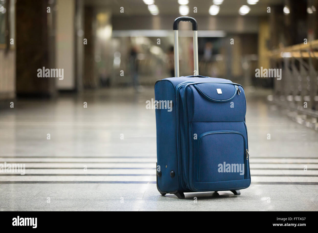 Large blue wheeled suitcase standing on the floor in modern airport terminal. Copy space Stock Photo