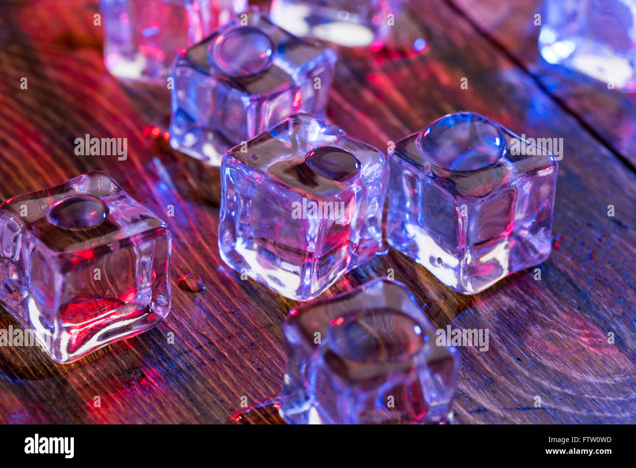 Cold and wet ice cubes with colorful light on wooden table Stock Photo