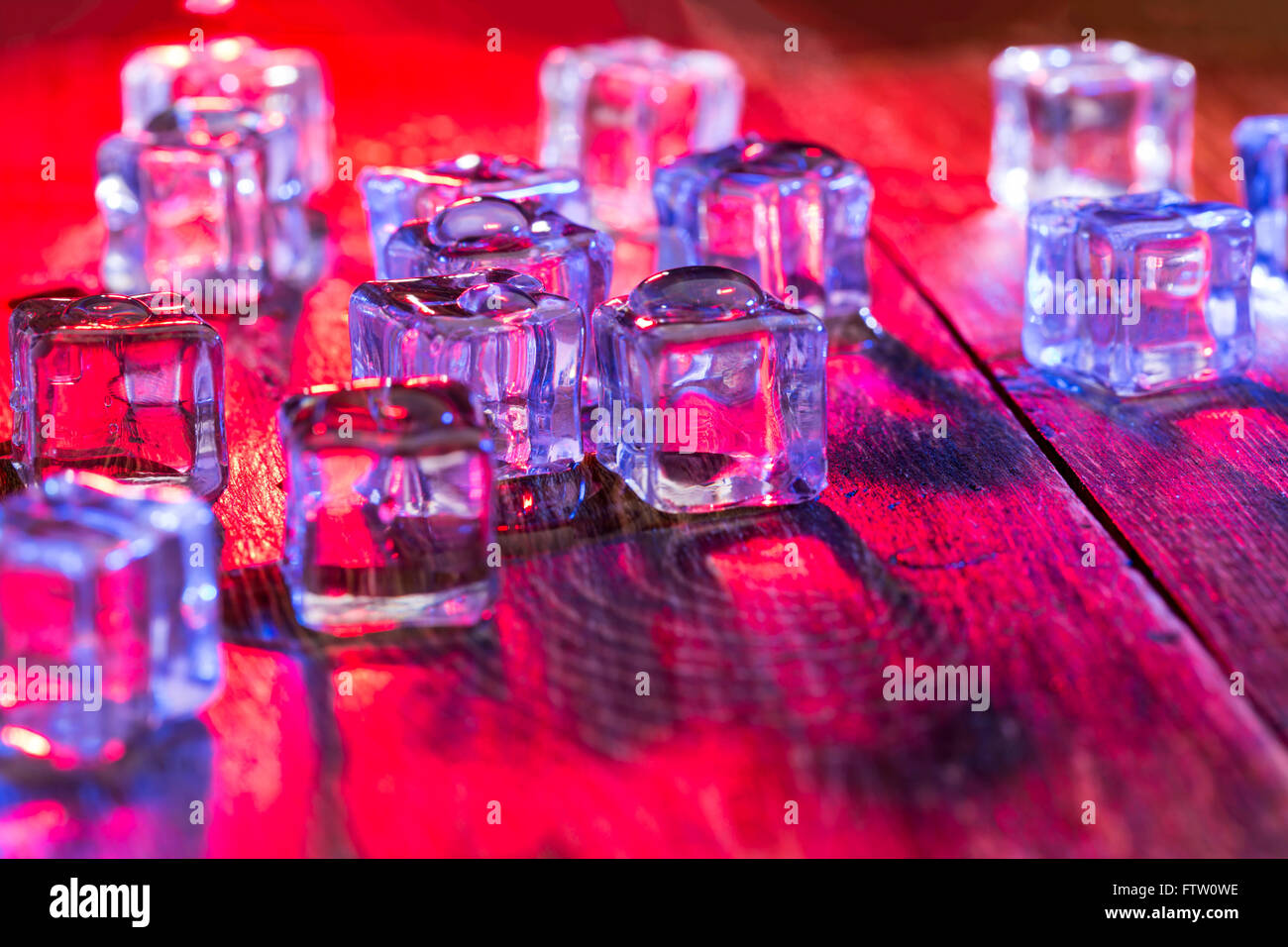 Cold and wet ice cubes with colorful light on wooden table Stock Photo