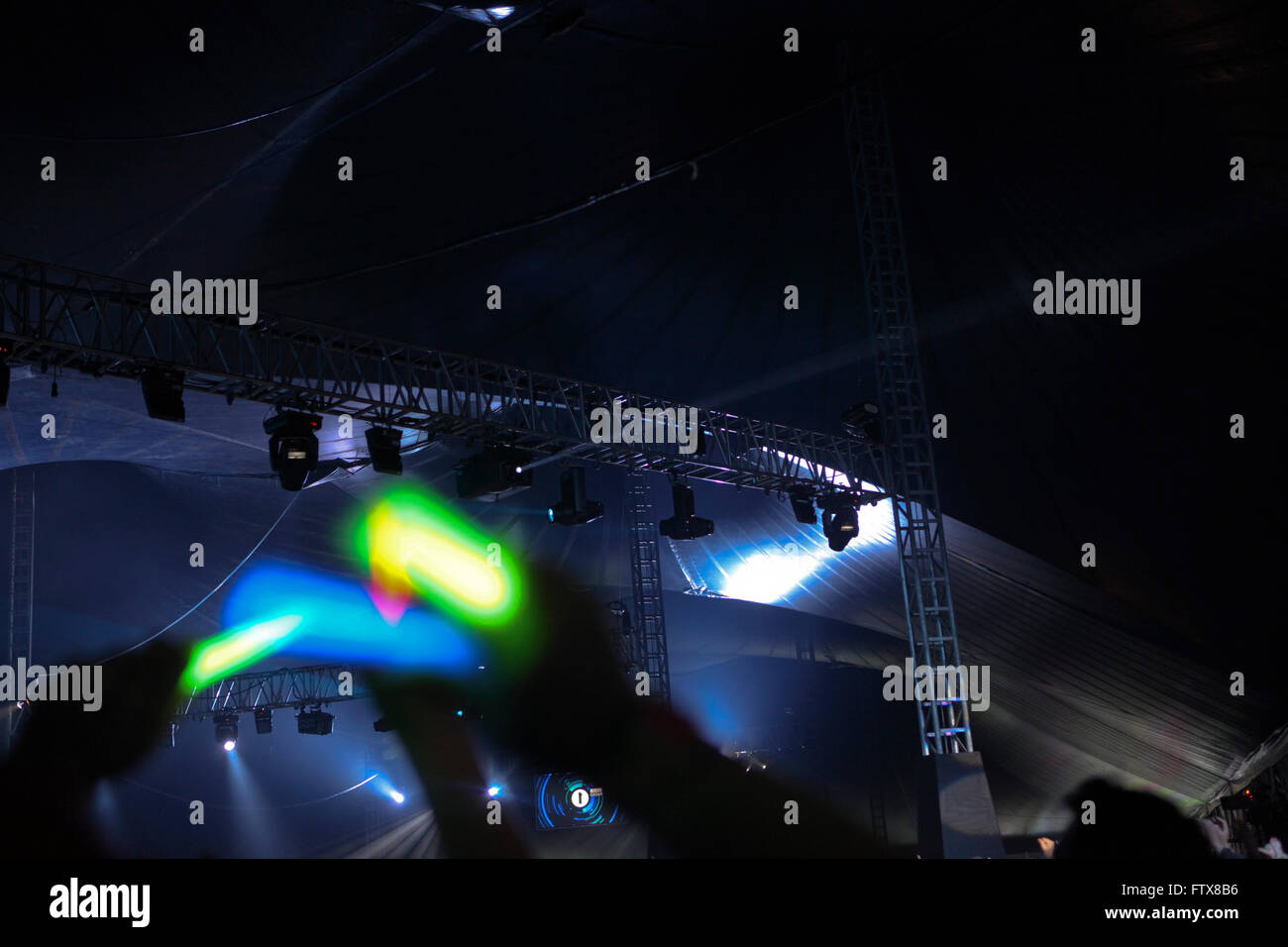 Crowds of music lovers wave glow sticks above their heads in time to the music underneath the huge tented arena pof an open air festival, concert or gig. Stock Photo