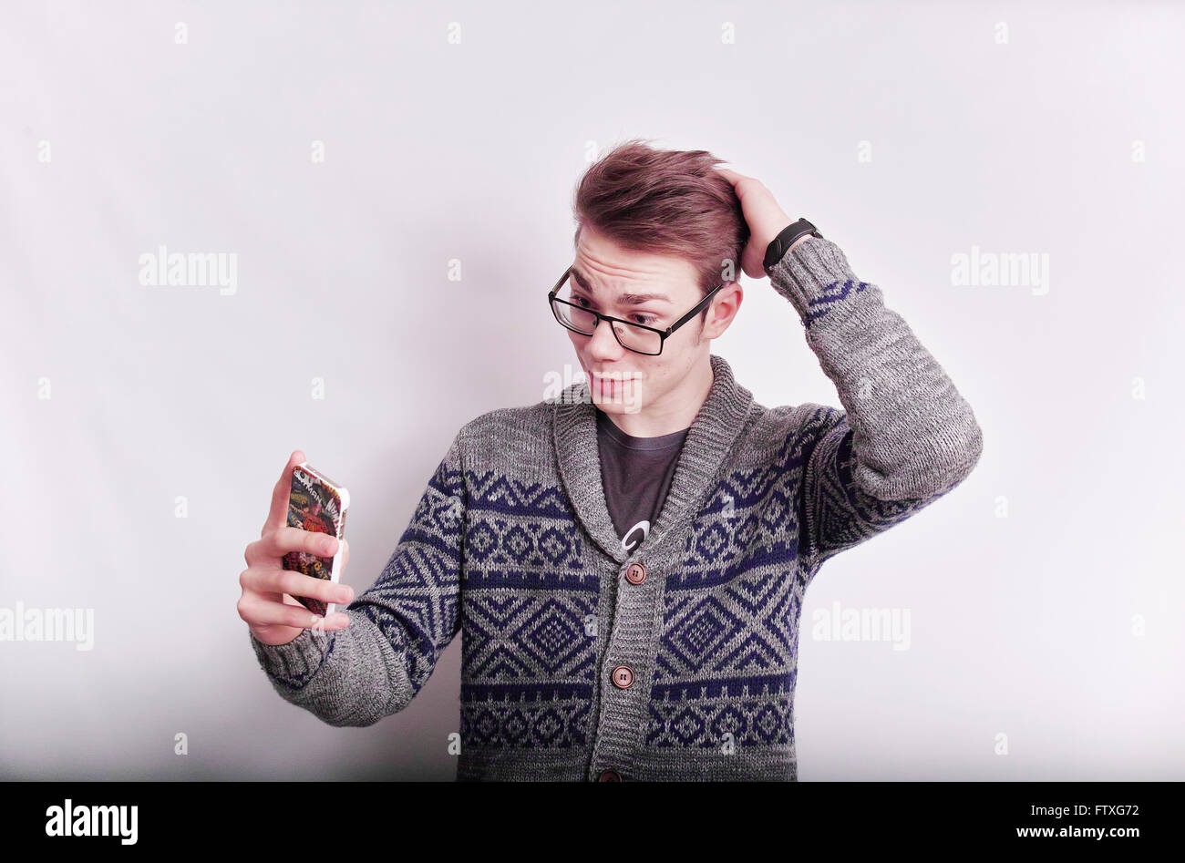 Young man wearing glasses, taking a selfie with a mobile phone while posing with hand on head. Stock Photo