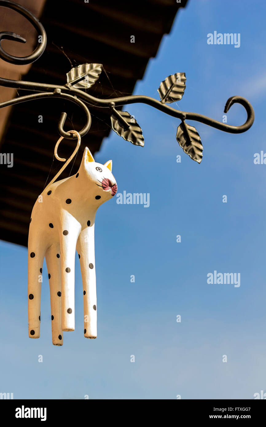 Wooden figurine of cat hanging at entrance to house on blue sky background Stock Photo