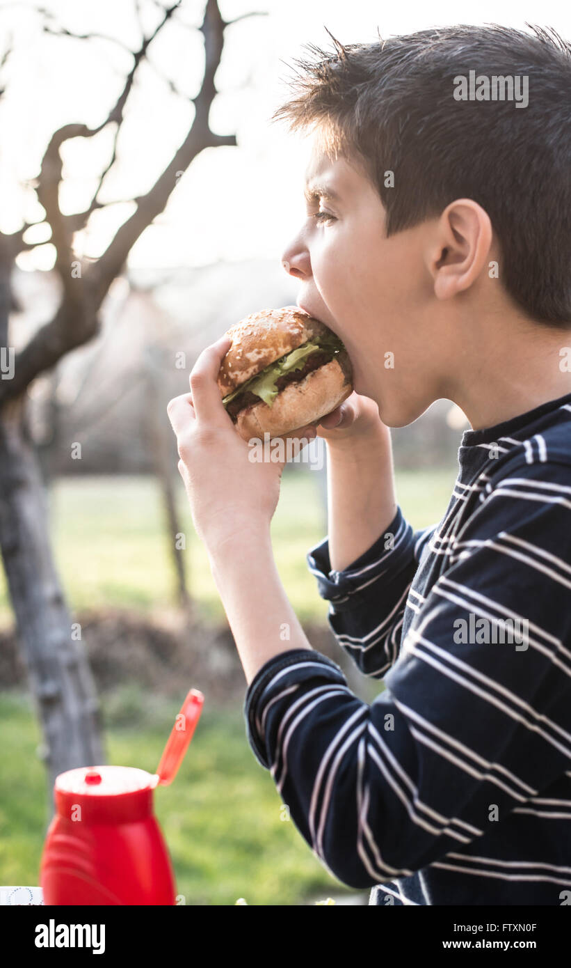Boy eating hamburger in garden Stock Photo