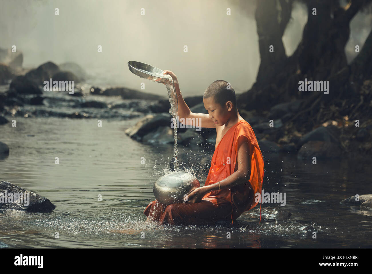 Novice monk sitting in creek cooling off Stock Photo